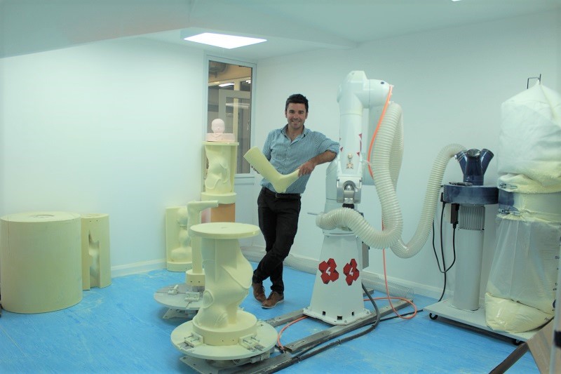 Sam Walmsley stands next to Victor the Rodin4D robot and orthotic moulds milled out by the machine.