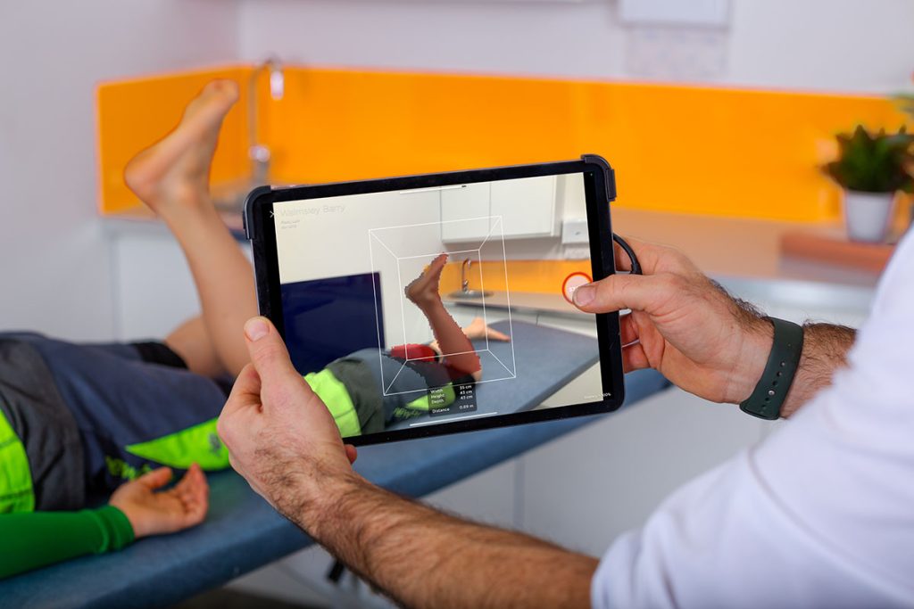 Orthotist scanning the ankle and foot of a child using 3D scanning software during a clinical appointment