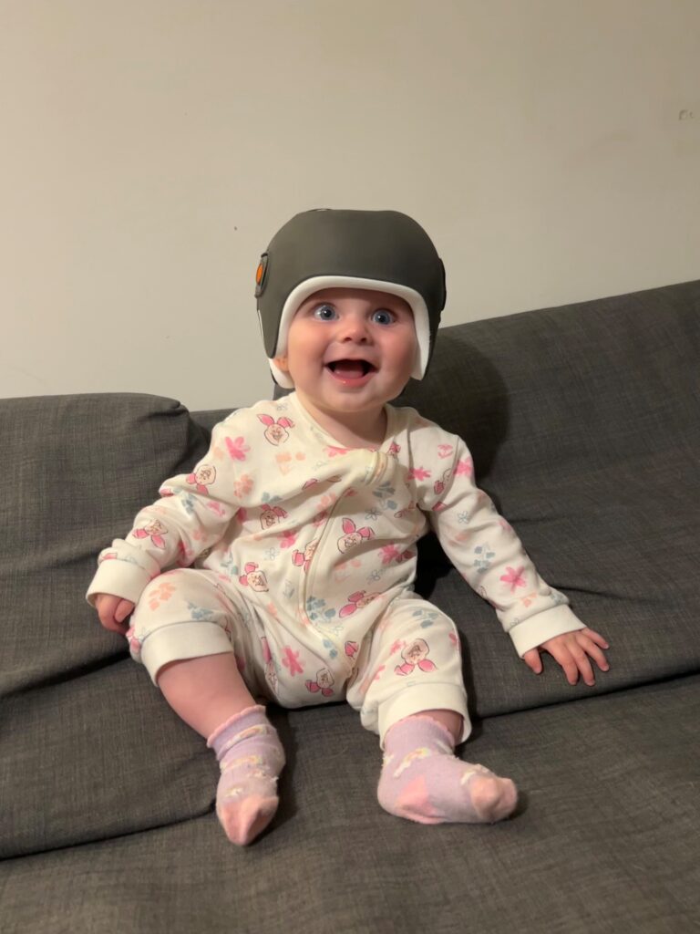 Lexie sitting on a sofa, smiling while wearing her LOCband Lite helmet